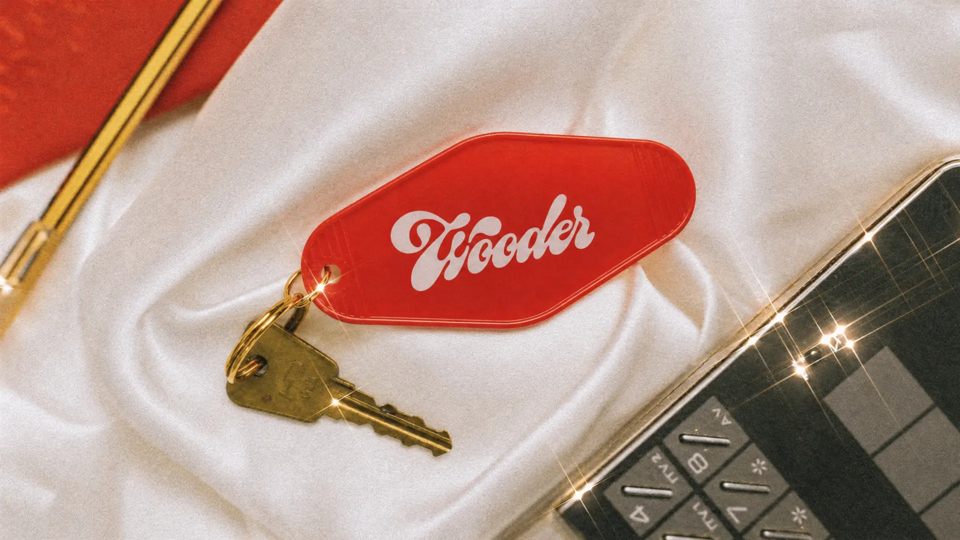 Red Wooder motel key tag with brass keys resting on white satin